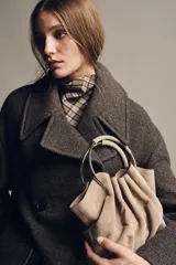 Bolso tipo saca de serraje color beige con doble asa rígida asimétrica y asa bandolera extraíble. Incluye cartera con bolsillo extraíble.