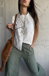 Camisa sin mangas blanca de broderie, con cuello alto fruncido y cierre frontal con botones.