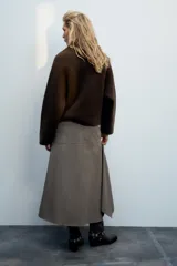 Chaqueta de punto marrón de textura bouclé, con cuello subido, manga larga ancha y cierre frontal oculto con cremallera.