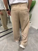 Pantalón sastrero de corte recto y holgado, color beige, con pinzas frontales y bolsillos laterales.