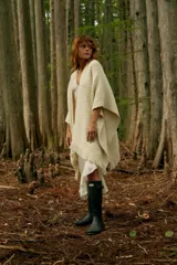 Ruana color crema de tejido de punto grueso con flecos en el borde inferior.