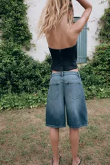 Bermuda baggy de denim azul con tiro medio, trabillas para cinturón y diseño de cinco bolsillos. Presenta cierre frontal con cremallera y botón metálico.
