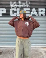 Campera con capucha y cierre frontal de Nude Project, color marrón, con corte boxy y diseño oversized. Presenta un parche bordado en relieve con las iniciales NP en el pecho, capucha amplia y bolsillos tipo canguro.