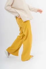 Pantalón ancho de color mostaza con costuras contrastantes en blanco. Presenta un corte recto y aberturas en los bajos delanteros.