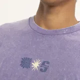 Remera color beige de corte holgado con estampado pequeño en el pecho de una flor y la letra S.