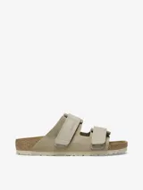 Sandalia Birkenstock modelo Uji en color taupe, confeccionada con una parte superior de gamuza suave y correas de nobuk con cierre de velcro. Presenta la clásica plantilla anatómica de corcho y suela de EVA.
