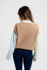 Cárdigan de punto color crema con mangas largas y terminaciones en color naranja y lila. Posee cuello en V y cierre frontal con botones color madera.