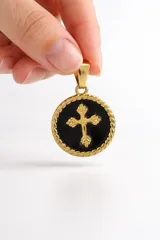 Dije circular de acero dorado con borde trenzado y centro esmaltado en color negro, que presenta una cruz dorada con diseño floral en relieve.
