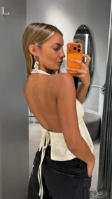 Top halter de tejido de punto color blanco, con escote en V pronunciado, diseño abierto en el frente y bajo asimétrico en punta.