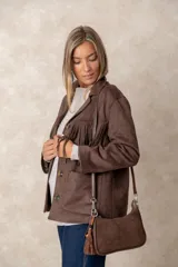 Cartera tipo baguette color marrón chocolate, confeccionada en una combinación de texturas de cuero y gamuza. Cuenta con una correa larga ajustable, cierre superior y un detalle decorativo de borla colgante con cuentas en el lateral.