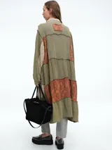 Vestido camisero de corte midi con diseño patchwork que combina paneles en tonos crudo y marrón con estampados florales sutiles. Presenta cierre frontal con botones, cuello camisero y mangas largas con puños.