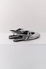 Balerina negra de cuero con punta fina y dos correas marrones con hebilla sobre el empeine. Decorada con tachas plateadas.