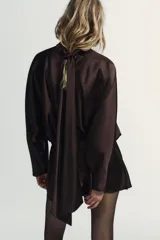 Vestido corto de tejido satinado color marrón chocolate, con cuello subido y lazada tipo foulard integrada. Presenta mangas largas amplias, detalle de frunces en la cintura y cierre lateral con cremallera oculta.