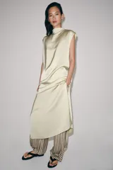 Vestido midi de Zara Woman Collection confeccionado en hilatura de viscosa con tejido satinado, de color beige. Presenta cuello subido, diseño sin mangas (manga sisa), bajo recto con aberturas laterales y cierre en la espalda con alamares.