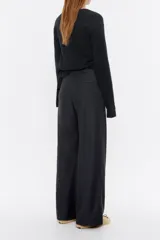 Pantalón largo negro de denim, corte amplio, con cierre frontal con corchete oculto y cremallera, y bolsillos laterales. Contiene 20% de fibras recicladas.