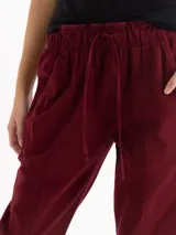 Pantalón de gabardina color bordó, de tiro medio con cintura elastizada y cordón regulable. Presenta calce relajado, corte recto y largo hasta los tobillos, con bolsillos laterales.