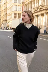 Jersey de punto negro, con cuello en V (pico) y manga larga, acabado en rib en puños, cuello y bajo.