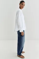 Blusa blanca confeccionada en lino, con cuello polo, escote en V y mangas largas amplias. Presenta un diseño holgado y bajo asimétrico.