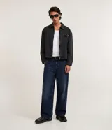 Pantalón de jean corte super baggy, de calce holgado y tiro alto. Presenta un diseño de cinco bolsillos, cierre frontal con botón y cremallera, y trabillas para cinturón. Confeccionado en algodón con un acabado de lavado marmoleado que le otorga un aspecto vintage.
