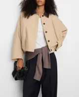 Chaqueta boxy acolchada de algodón en color beige, con cuello italiano de piel ovina en contraste, manga larga con hombro caído y bajo abullonado. Cuenta con cierre de botones y bolsillos de vivo inclinados en el delantero.
