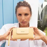 Billetera larga marca Lincoln's, color beige, con solapa frontal con cierre magnético y correa de mano integrada. Presenta una textura granulada y el logo de la marca grabado en la parte frontal.