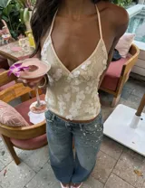 Top halter color champagne, con escote en V profundo y espalda descubierta. Está confeccionado con tela brillante y bordado de lentejuelas formando diseños florales en relieve.