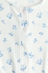 Cardigan ajustado de punto pointelle en color blanco, con pequeño estampado floral azul, escote redondo y cierre frontal de botones con ribetes de picot.