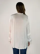 Camisa de satén color negro con cuello mao y volados en las mangas. Presenta cierre frontal con botones y diseño de corte holgado con largo asimétrico.