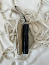Billetera de tamaño intermedio con diseño acolchado y acabado brillante. Cuenta con cierre metálico perimetral y una correa de muñeca extraíble con dije metálico circular grabado.