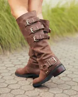 Botas de caña alta confeccionadas en cuero color marrón caoba. Presentan un diseño robusto con tres hebillas metálicas ajustables en el lateral superior y una correa con hebilla y remaches metálicos en la zona del tobillo. Cuentan con un taco bajo cuadrado y suela de goma resistente.