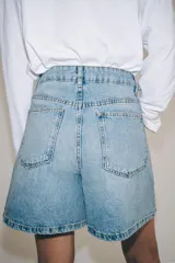 Shorts denim de tiro alto y corte relaxed, confeccionados en tejido vaquero celeste claro. Presentan trabillas en la cintura, diseño de cinco bolsillos, pliegues frontales y cierre con cremallera y botón metálico.