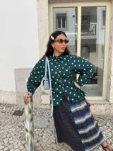 Camisa negra de popelina con diseño de flor azul estampada en el frente. Presenta cuello clásico, mangas abullonadas y detalle de cordones laterales tipo corset para ajustar la silueta.
