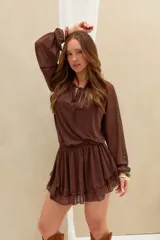 Vestido corto marrón de tejido semitransparente, con mangas largas abullonadas, escote redondo con cordones para ajustar y falda con volados en capas.