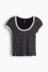 Top corto de manga corta, ajustado al cuerpo, con estampado floral pequeño en blanco sobre fondo negro. Presenta ribete de encaje blanco en el escote redondo y en los bordes de las mangas. El cuerpo principal parece ser de tejido acanalado.