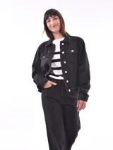 Campera de jean negra, estilo trucker, con cuello camisero, botones metálicos y bolsillos frontales con tapa.