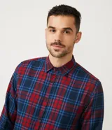 Camisa masculina de franela a cuadros en tonos rojo y azul, de corte comfort, con cuello camisero, manga larga y abotonadura frontal.