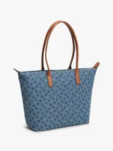 Cartera tote Tommy Hilfiger confeccionada en tejido denim azul con estampado geométrico de monogramas. Cuenta con asas superiores de cuero sintético marrón, cierre superior de cremallera y herrajes metálicos dorados con el monograma de la marca en el frente.