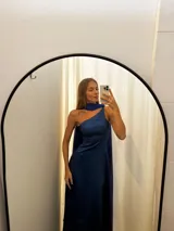 Vestido largo de tafeta con brillo, color verde, de corte al cuerpo y escote asimétrico de un solo hombro. Incluye una pieza de seda liviana drapeada sobre el hombro opuesto.