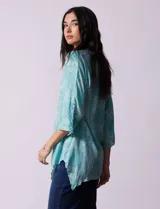 Camisa celeste con estampado de cachemir en blanco, cuello a la base, escote en V y abertura central con botones. Terminación de ruedo asimétrico. Manga 3/4 de largo regulable con presilla y botón.