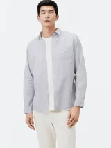 Camisa de manga larga con cierre frontal de botones, cuello clásico y bolsillo en el pecho. Presenta un diseño de rayas verticales finas en tonos azul y blanco.
