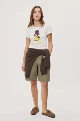 Remera blanca de manga corta, con estampa frontal de un pato de hule con turbante y labios pintados, acompañada de la frase "In all else fails, denial".