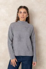 Buzo de punto gris con cuello alto, manga larga y diseño holgado. Presenta un sutil bordado floral en relieve al tono en la parte frontal.