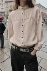 Cuerpo de cuello subido y manga larga, con cierre frontal de botones. Presenta detalles de costuras a contraste, bolsillos delanteros y acabados elásticos en puños y ruedo.