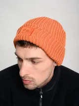 Gorro tipo beanie de tejido acanalado en color azul, con parche rectangular rojo en el frente que presenta el logo de la marca Umbro bordado en blanco.