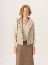 Chaleco con capucha, presenta una espalda de pelo sintético en color marrón oscuro con etiqueta de cuero negra y una capucha de tela tipo denim azul. Diseño original con mezcla de texturas.