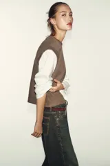 Prenda de manga larga blanca con un chaleco de tejido de punto azul marino superpuesto, creando un efecto de dos piezas. El chaleco es de cuello redondo y corte recto.