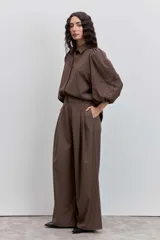 Pantalon de vestir color marron, de corte sastrero con piernas anchas y tiro alto. Presenta pinzas frontales y bolsillos laterales.