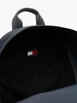 Mochila de diseño redondeado en color gris, con compartimento principal amplio, bolsillo frontal con cierre y parche distintivo de la marca en la parte inferior. Cuenta con asa superior y correas acolchadas ajustables.