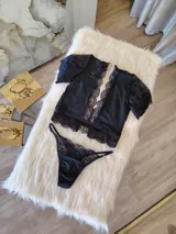 Conjunto de lencería compuesto por un top bralette y una tanga. El top presenta un diseño con escote profundo, mangas cortas de encaje y detalles de encaje en los bordes. La tanga es de corte regulable, confeccionada en lycra y encaje con forro de algodón.