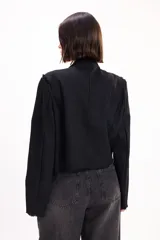 Chaqueta negra de estilo militar con detalles de cordones soutache en el frente, solapas clásicas y cierre frontal con ganchos.